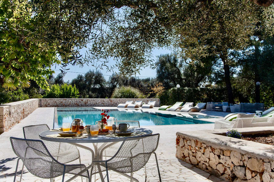 Outdoor dining area by a pool with lounge chairs and greenery
