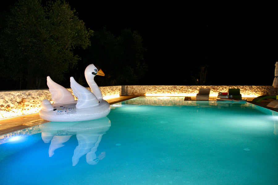 Inflatable swan pool float in a pool at night with lights reflecting on water