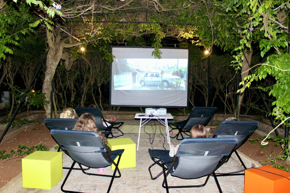 Outdoor movie night setup with people watching a screen in a garden.